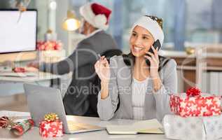 Christmas is here and the office is filled with cheer. a young businesswoman using a laptop and smartphone in a modern office at Christmas.