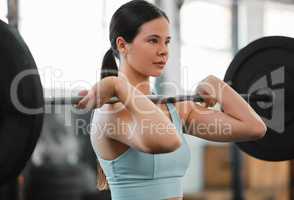 A fit, active and muscular bodybuilder female lifting weights in the gym exercising to improve strength and conditioning. Young woman athlete training with a barbell as part of her workout routine