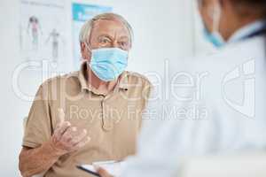 I have some concerns. a senior man sitting with his doctor and wearing a face mask during his consult in the clinic.