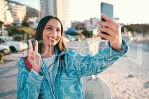Fun, happy and trendy student taking a selfie on phone for social media while exploring, visiting or enjoying city. Stylish, edgy and funky woman showing peace sign, symbol and gesture for social app