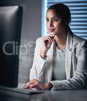 Systems seem to be running smoothly. an attractive young businesswoman sitting alone in the office at night and looking contemplative while using her computer.