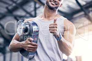 Regular exercise can do wonders for you. Closeup shot of a muscular young an holding a scale and showing thumbs up in a gym.