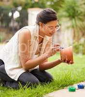 Creativity doesnt wait for that perfect moment. s young woman painting a pot in the garden at home.