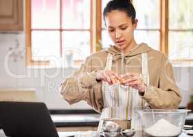 Only two eggs are needed. a young woman cracking an egg into a bowl while using her laptop to look up recipes.