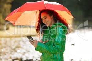 Nature called and shed love to have spend quality time with you. a beautiful young woman using a smartphone outside in the rain.