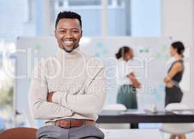 Confidence is the best asset for success. Portrait of a confident young businessman posing with his arms crossed in an office with his colleagues in the background.