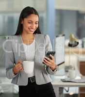 Right on time as always. a young businesswoman using a smartphone and having coffee in a modern office.