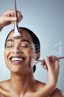 Being pampered. Studio shot of an attractive young woman having her makeup done backstage against a grey background.