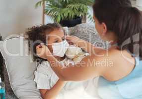 Health care for sick, tired little girl with covid wearing face mask while resting on a sofa at home with worried mother. Anxious parent helping her unwell daughter to protect and stop virus spread