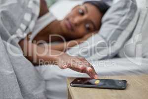 Its time to wake up. a womans alarm on her cellphone going off while she lies in bed.
