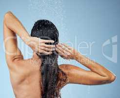 Wash your hair regularly for optimal scalp and hair health. Studio shot of an attractive young woman washing her hair while taking a shower against a blue background.