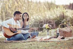 Sharing my love through music. Full length shot of a young woman sitting with her boyfriend while he plays the guitar during their picnic date.