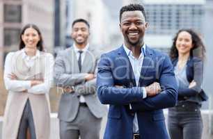 Confidence comes from what you do in practice each day. Portrait of a confident young businessman standing with his arms crossed in the city with his colleagues in the background.