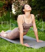 Yoga is about putting your mind and body at ease. a young woman doing a cobra stretch while exercising outdoors.