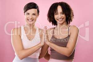 High fives for fitness. Cropped portrait of two attractive young female athletes meditating in studio against a pink background.