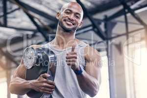 Physical activity will always be a part of my life. Portrait of a muscular young an holding a scale and showing thumbs up in a gym.