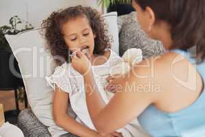 Sick child drinking medicine, soup or food lying on the sofa for health and recovery inside their home. Ill girl being fed from a spoon by caring, loving and affectionate mother feeding her