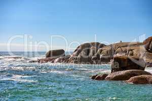 Big boulders, rocks and stones at the beach, sea and ocean against a clear blue sky background with copy space. Calm, majestic and scenic landscape view across the horizon and rocky coast in summer