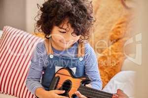 Listen to me play. a little boy playing the guitar while sitting at home.