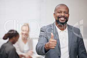 Stay optimistic and you will succeed. Portrait of a mature businessman showing thumbs up in an office with his colleagues in the background.