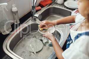 Learning to be responsible. an unrecognizable girl standing and washing the dishes in the kitchen sink at home.