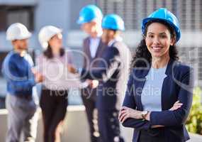 Were ready to build the empire you want. a young businesswoman standing with her arms folded and wearing a hardhat while her colleagues stand behind her.