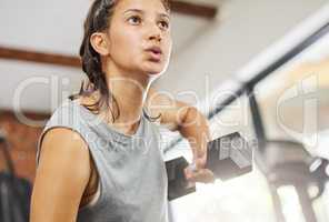 Lift weights and train hard. Low angle shot of a sporty young woman exercising with a dumbbell in a gym.