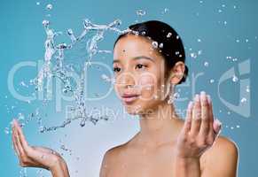 The skin needs extra moisture as we age. an attractive young woman posing against a blue background in the studio and splashing her face with water.