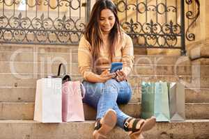 You wont believe the deals Ive found. Full length shot of an attractive young woman taking a break from shopping to send a text message.