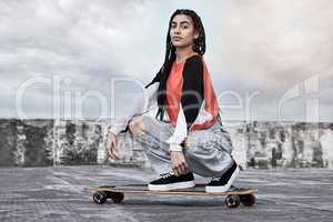 Unbeatable on the board. Cropped portrait of an attractive young female skater crouching on her longboard on a rooftop against a stormy backdrop.