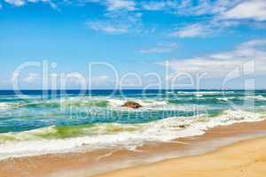 Ocean waves, turbulent sea and rough tides from strong winds crashing onto a boulder at the beach shore with a cloudy blue sky copy space background. Rocky seaside view, landscape and coastal scenery