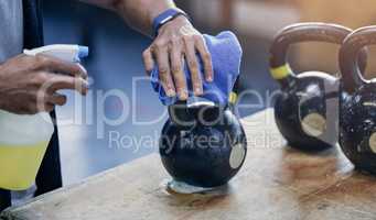 Reducing risk of infection so you can exercise safely. Closeup shot of an unrecognisable man sanitising a kettlebell while working in a gym.