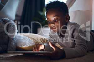 Nighttime is the best time to read. a little boy using his digital tablet while lying on the floor.