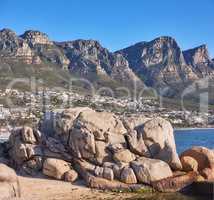 Beautiful, nature view of the beach front or rocky boulder on the seashore against a mountain landscape and blue sky on a Summer day. Calm scene of the beach and the ocean in the city.