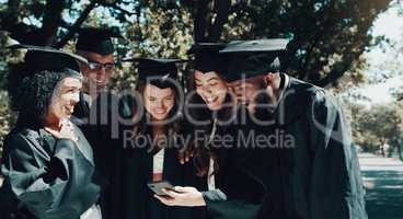 Look at all the likes were getting. a group of students looking at something on a cellphone on graduation day.