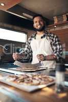 Your pizza is almost ready. a handsome young man standing and preparing a freshly made pizza for takeaway in his restaurant.