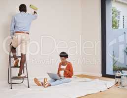 Taking the weight of my feet while he paints. Full length shot of a young couple redecorating a room at home with fresh paint.