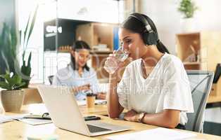 Its important to keep hydrated. a young businesswoman drinking a glass of water at work.