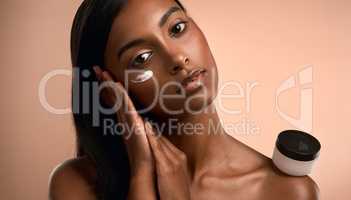 We cant lose touch but we can let go. Portrait of an attractive young woman applying moisturiser against a brown background.