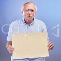Can I speak to the complaints department. Studio shot of a senior man holding a blank sign and looking unhappy against a blue background.
