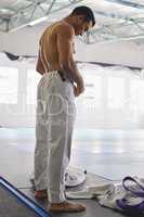 Today, he worked up a sweat. Rearview shot of a handsome young man standing shirtless in his jiu jitsu pants in the gym.