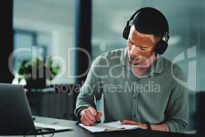 Music gives me motivation to get through the day. a young businessman writing on a notepad in an office at work.