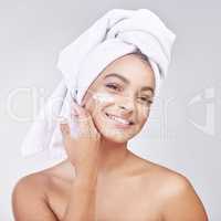 Invested time, youthful skin. Studio shot of a beautiful young woman applying moisturiser against a grey background.