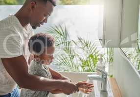 Maintaining good hand washing techniques and habits. a father helping his son wash his hands at a tap in a bathroom at home.