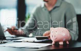 Try not to break the piggybank when spending money. an unrecognizable businessman doing paperwork with a piggybank on his desk at work.