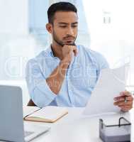 Sorting business matters. a young businessman going through paperwork while working on a laptop in an office.