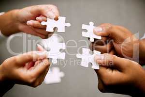 Together we can find the perfect solution. Closeup shot of a group of unrecognizable businesspeople holding puzzle pieces together.