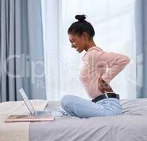 Be aware of your posture. Full length shot of an attractive young woman holding her back in pain while working on her laptop in the bedroom at home.