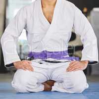 Your bely highlights your progress. an unrecognizable young man kneeling in full jiu jitsu gi in the gym.