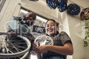 Leave the fixing to us. Low angle shot of two young business owners standing together in their bicycle shop and holding spare parts.